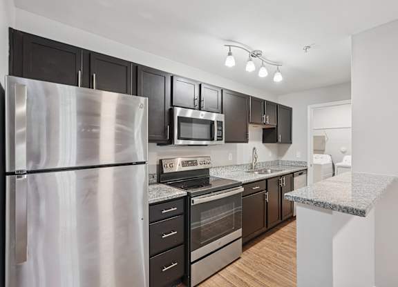 A kitchen with a refrigerator, microwave, oven, and sink.