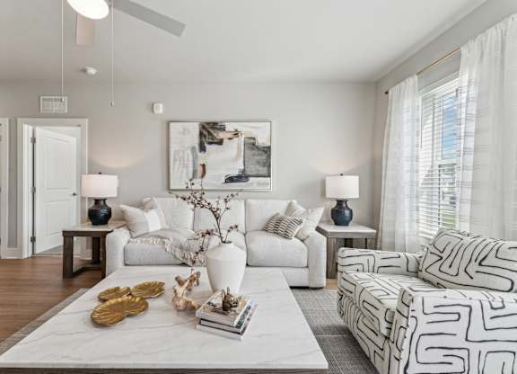 A living room with a white sofa, a grey armchair, and a coffee table with a vase and books on it at The Hendry Apartments, Fort Myers, FL, 33905