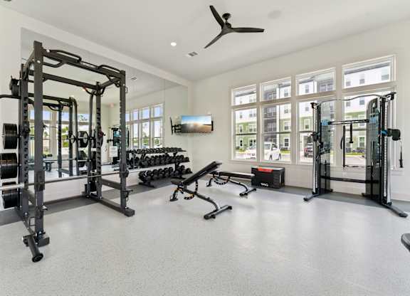 A spacious gym with a variety of equipment including a squat rack, bench, and weights at The Hendry Apartments, Fort Myers, FL