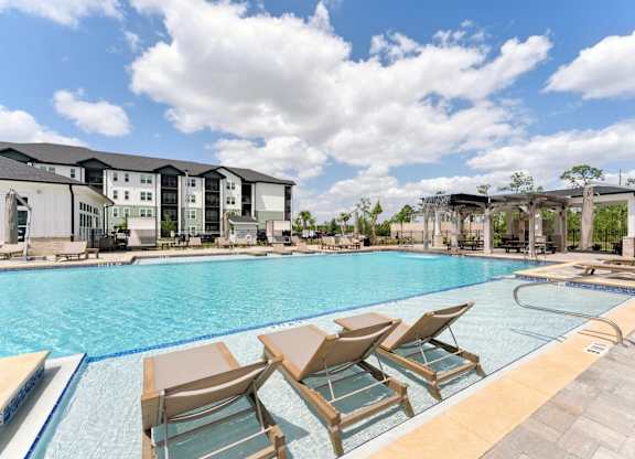 A pool with chairs and a building in the background at The Hendry Apartments, Florida, 33905