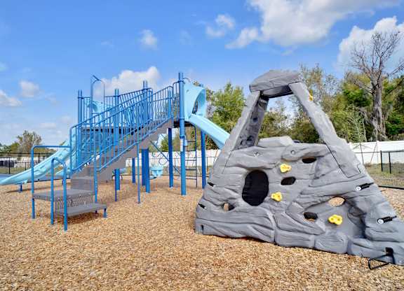 A playground with a blue slide and a grey rock climber.