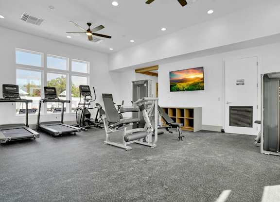 A spacious gym with a variety of equipment and a large window overlooking the outdoors.