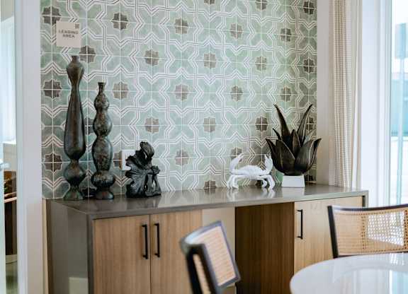A kitchen with a green and white tiled backsplash and a wooden table.