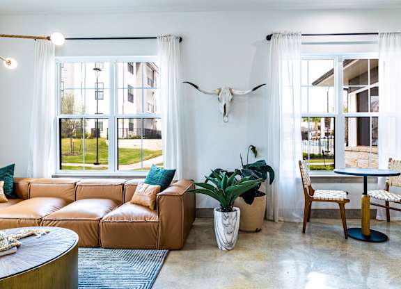 Living room with a leather couch and a table and windows at The Parker Austin, Pflugerville, Texas