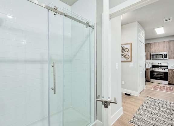 A glass shower door in a white bathroom at The Ashton at East Park Apartments, Kennesaw, 30144