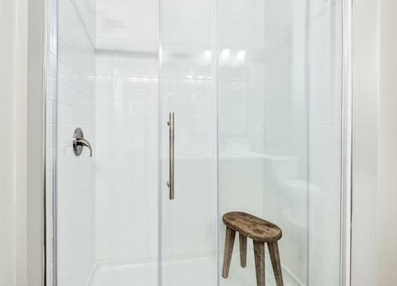 A wooden stool is in front of a glass shower door at The Ashton at East Park Apartments, Georgia, 30144