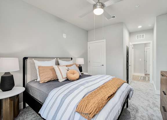 A bedroom with a bed, nightstand, and ceiling fan at The Ashton at East Park Apartments, Kennesaw