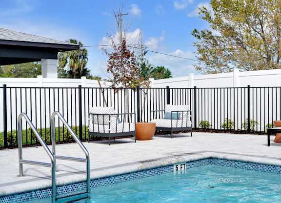 A pool with a ladder and chairs around it.