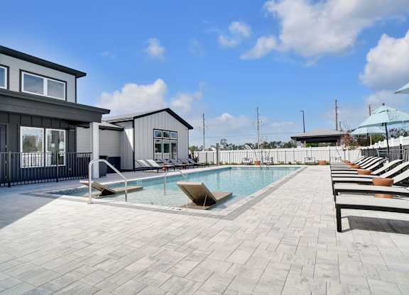 A pool area with sun loungers and a building in the background.