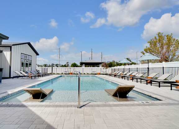 A large outdoor swimming pool with sun loungers and a building in the background.
