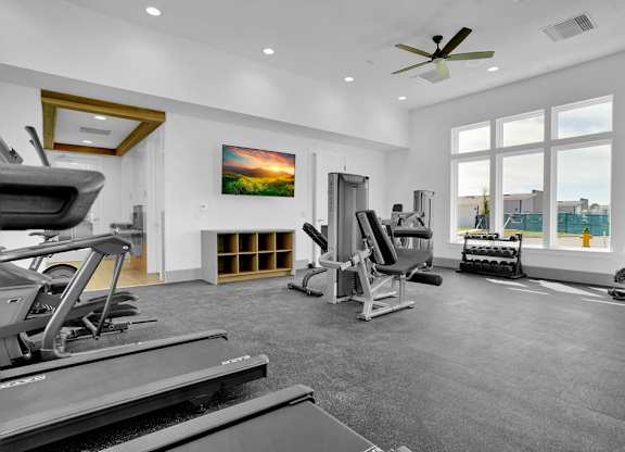 A spacious gym with treadmills, weights, and a ceiling fan.