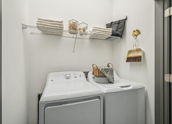 a washer and dryer in a white laundry room with a shelf above it at The Leo Myrtle Beach, South Carolina, 29579