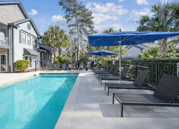 A pool with a blue umbrella and chairs.