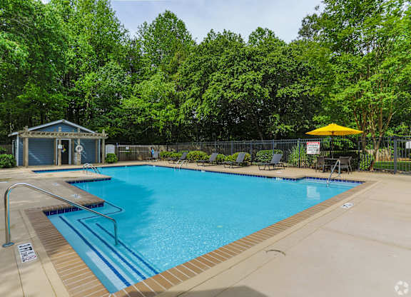 A pool surrounded by trees and a small building.