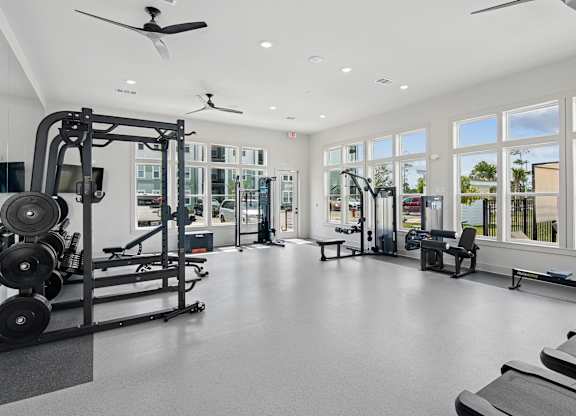 A spacious gym with a variety of equipment and a view of the outdoors through large windows at The Hendry Apartments, Florida