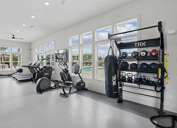 A TRX suspension trainer is hanging on a rack in a spacious room with a treadmill, exercise bike, and other workout equipment at The Hendry Apartments, Florida, 33905
