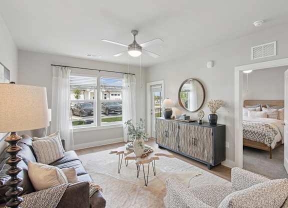A well-lit, spacious living room with a large window, a sofa, a side table, and a bed in the background at The Hendry Apartments, Fort Myers, 33905