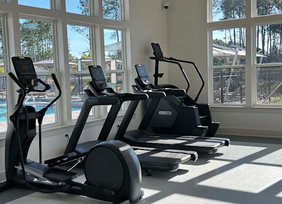 A row of elliptical machines are lined up in a sunny gym at The Beacon at 331 Apartments, Santa Rosa Beach, Florida