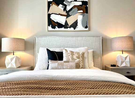 A bedroom with a large bed, two lamps, and a painting on the wall at The Collective Upper Westside Apartments, Georgia