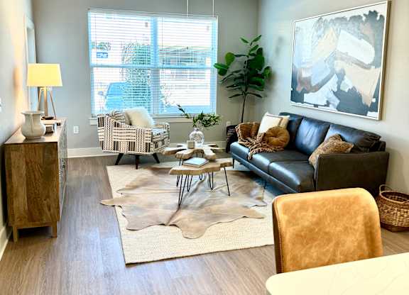 A living room with a brown leather couch, a wooden side table, a white table, and a rug at The Collective Upper Westside Apartments, Atlanta, GA, 30318