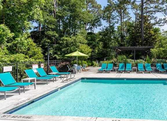 A pool surrounded by trees and lounge chairs.