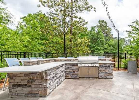 A stone barbecue area with a grill and chairs.