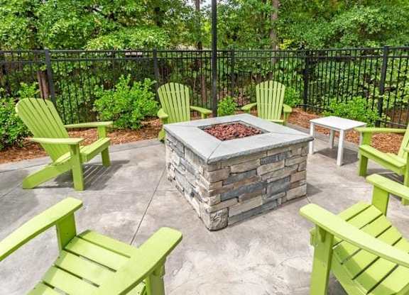 A fire pit surrounded by green chairs in a backyard.