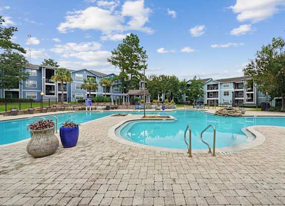 A swimming pool surrounded by a brick patio and apartment buildings.