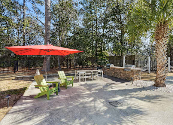 A patio with a red umbrella and green chairs.