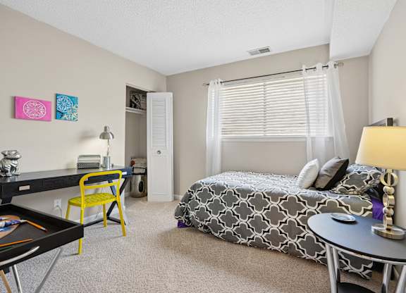 A bedroom with a bed, desk, chair, and a framed picture on the wall.