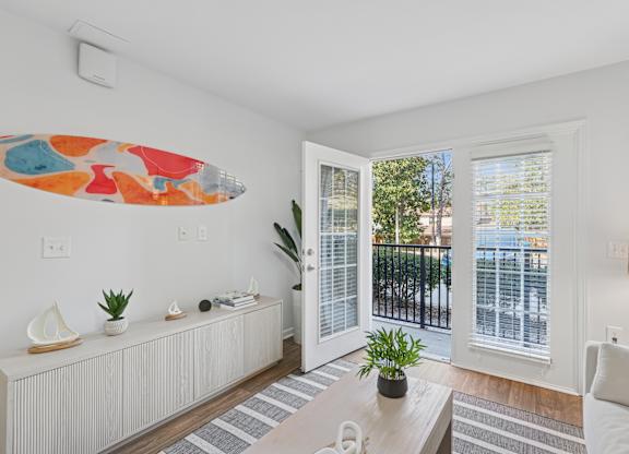 A living room with a white couch, a coffee table, and a surfboard artwork on the wall.