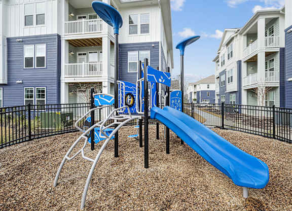 A playground with a blue slide and a black fence.at The Parker Leland, Leland