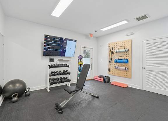 A gym room with a bench, weights, and a screen.