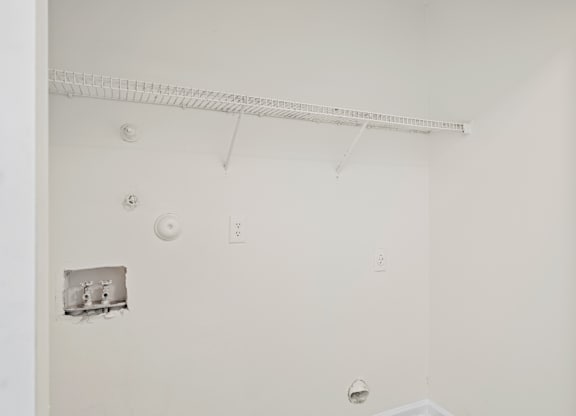 A white wall with a shelf and a few electrical outlets.