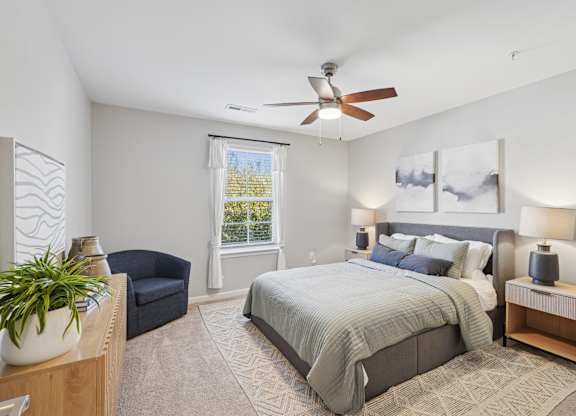 A bedroom with a large bed, a ceiling fan, and a window with a view of trees.