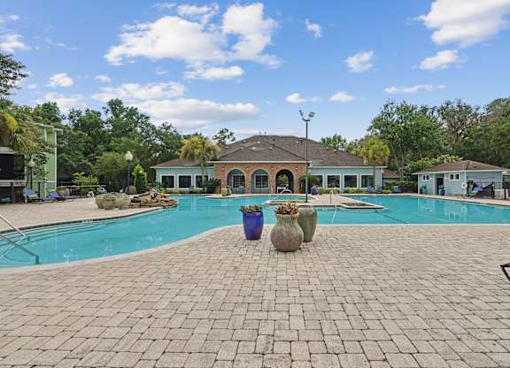 A pool surrounded by a brick patio with a blue sky and clouds in the background.