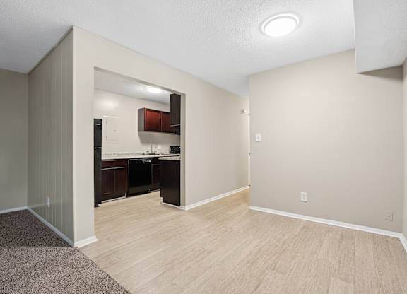 A room with a kitchen area in the background and a carpeted floor.