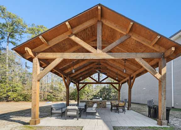 A wooden pavilion with a roof and a table and chairs underneath it.