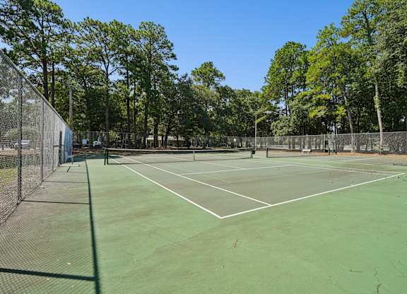 A tennis court surrounded by a fence and trees.