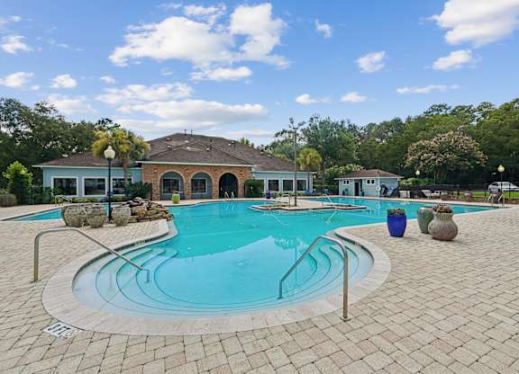 A swimming pool surrounded by a brick patio and a house in the background.