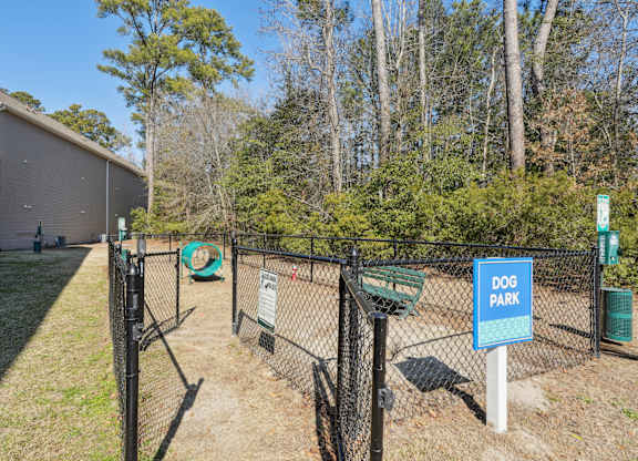 A dog park sign is on a fence in front of a building.