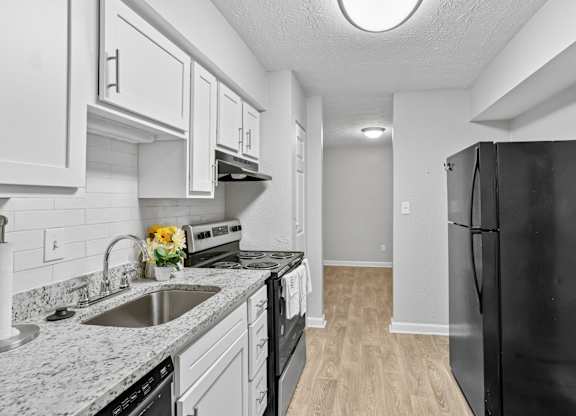 A black refrigerator is on the right in a kitchen with white cabinets.at Magnolia at Whitlock, Marietta, GA 30064