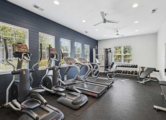 A spacious gym with treadmills, elliptical machines, and a fan.