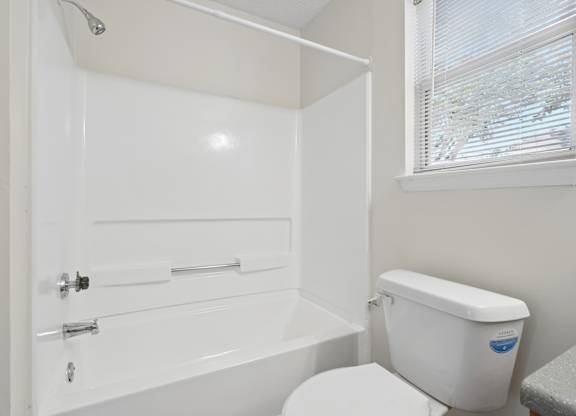 A white bathroom with a toilet, bathtub, and window.