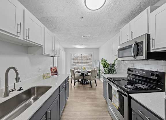 A kitchen with a stove, sink, and cabinets.