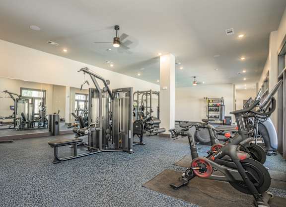 A gym with a variety of equipment including treadmills, weights, and a bench at The Ashton at East Park Apartments, Kennesaw, Georgia