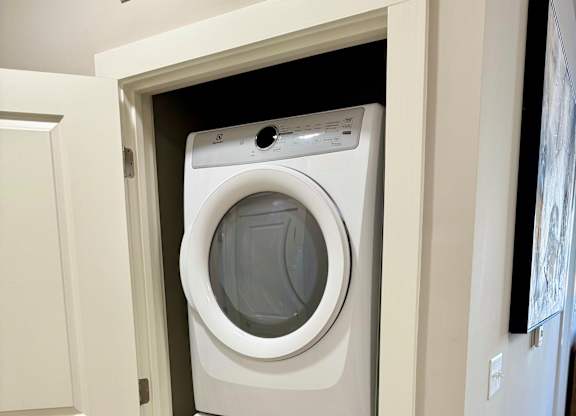 A white front load washing machine is in a white door at The Collective Upper Westside Apartments, Georgia, 30318