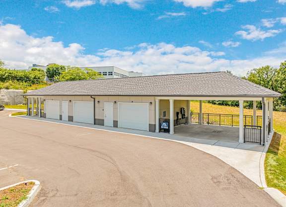 A large, open garage with a black roof and white walls is surrounded by a paved area and a metal fence at The Percy Apartments, Nashville