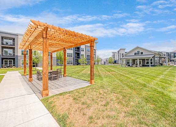 A wooden pergola is situated in a grassy area with a concrete walkway at The Percy Apartments, Tennessee