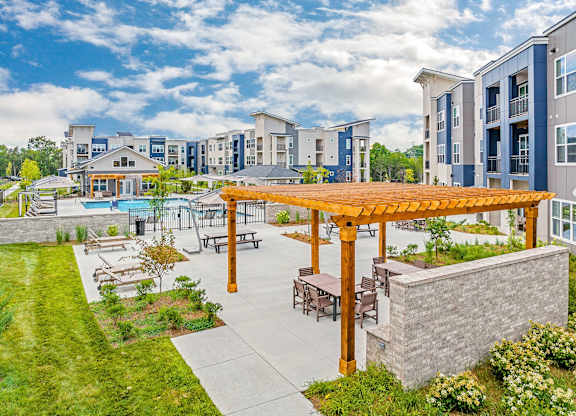 A large outdoor patio area with a wooden pergola and seating area in front of apartment buildings at The Percy Apartments, Nashville, TN, 37214